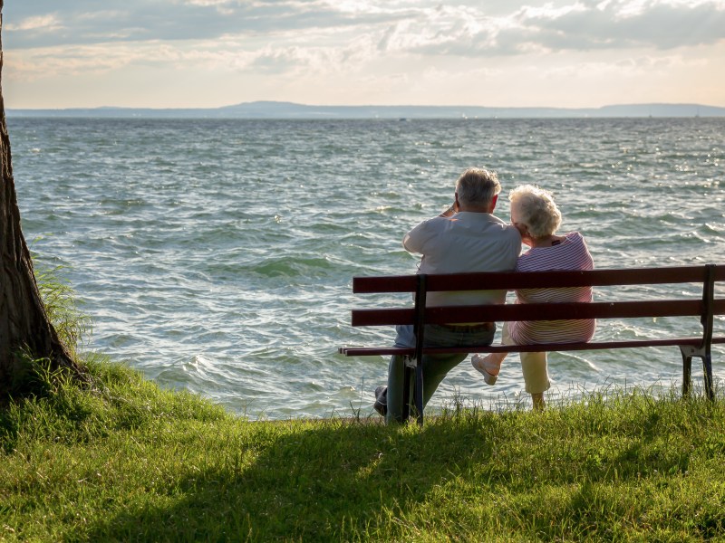 Ein Seniorenpaar sitzt an einem See auf einer Bank.
