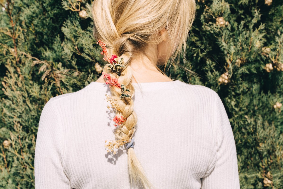 Blonde Frau mit Flechtfrisur und Blumen im Haar von hinten