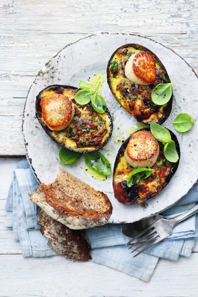 Gegrillte Avocados mit Jakobsmuscheln auf dem Teller angerichtet