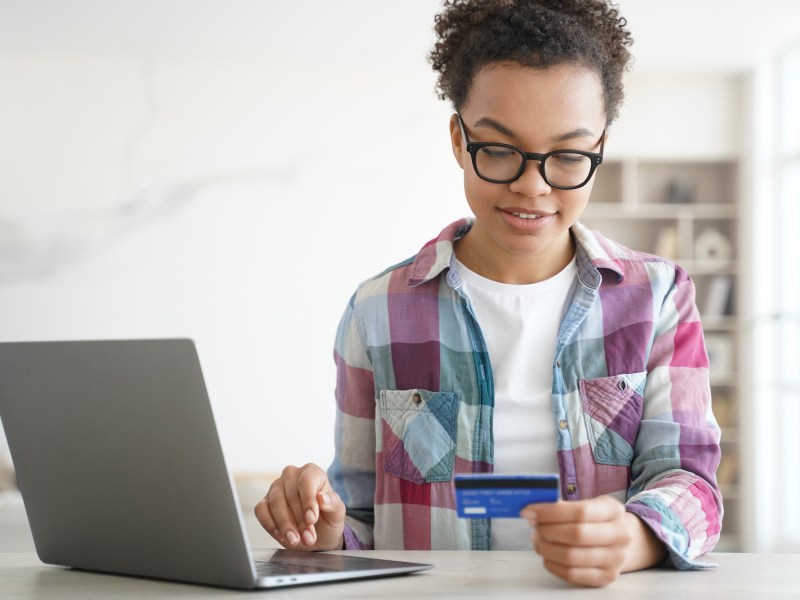 Eine Frau schaut auf ihre Bankkarte. Daneben ist ihr Laptop geÃ¶ffnet.