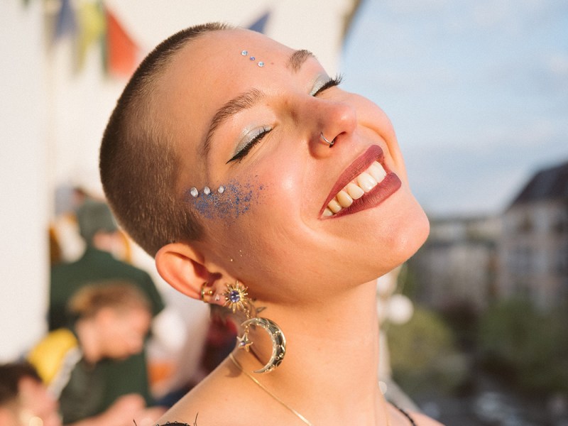 Frau mit rasierten Haaren lächelt und hat Glitzer Make-Up drauf