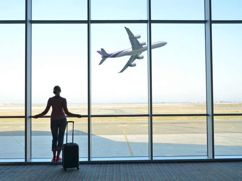 Frau steht mit Koffer am Flughafen