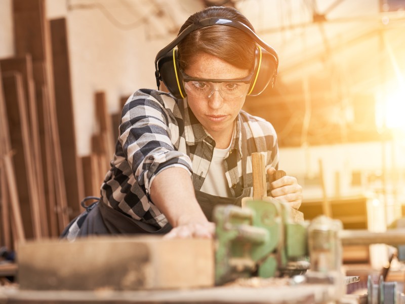 Eine junge Frau arbeitet in der Werkstatt. Sie sägt Holz.