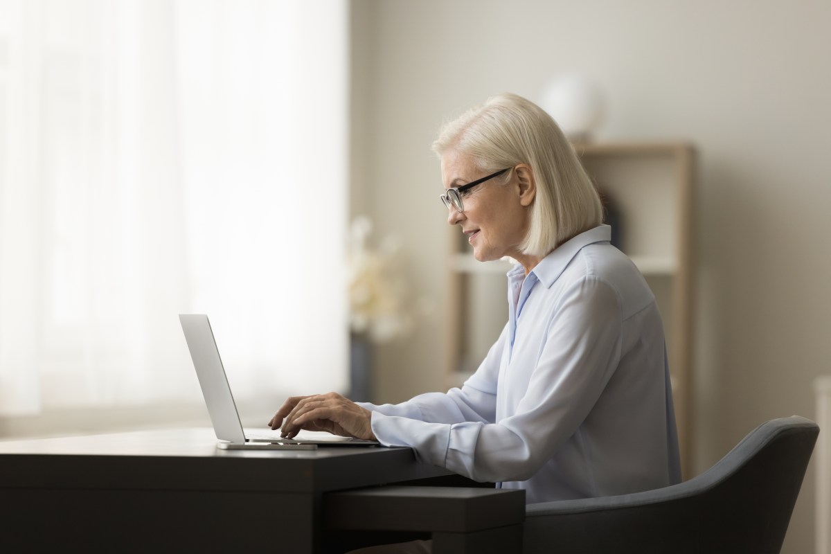 Eine ältere Dame mit weißen Haaren sitzt vor dem Laptop und arbeitet.