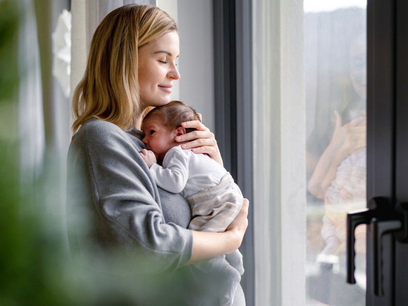 Eine Frau hält ein Baby auf dem Arm und schaut aus dem Fenster.