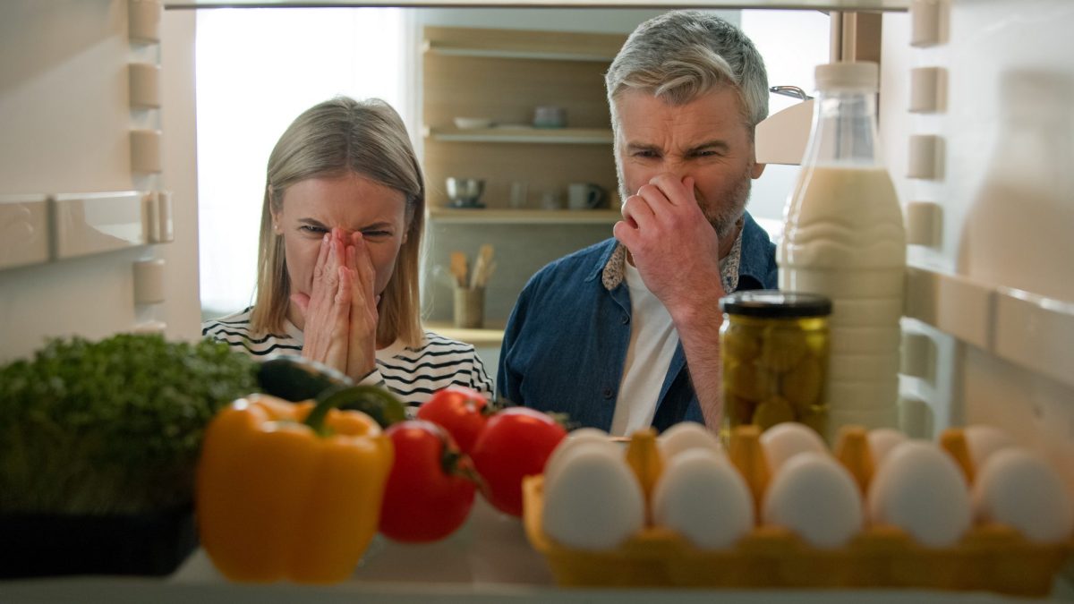 Mann und Frau halten sich vor dem Kühlschrank die Nase zu.