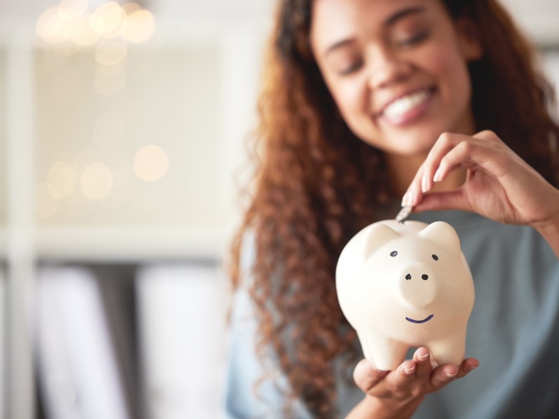 Eine junge Frau wirft eine Münze in ein Sparschwein.