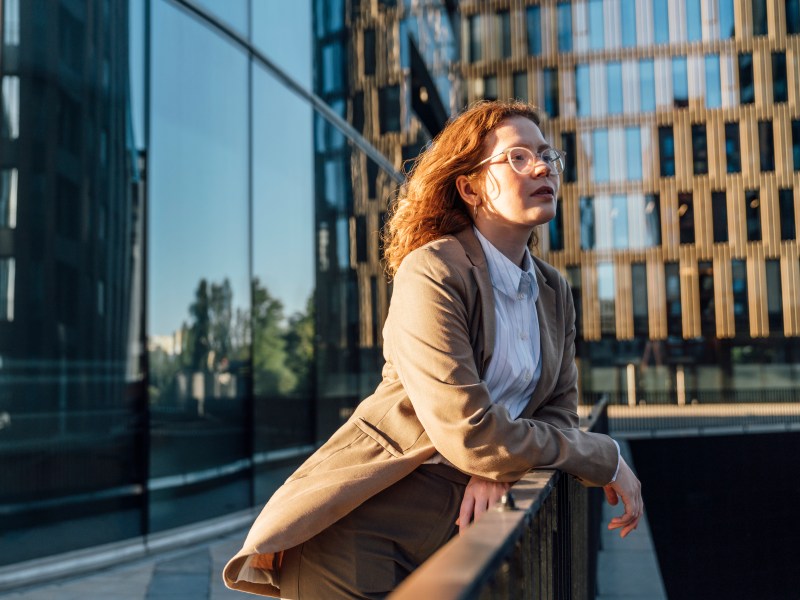 Nachdenkliche Geschäftsfrau mit Brille lehnt am Geländer