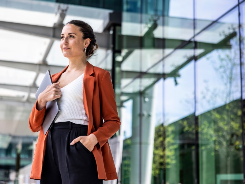 Geschäftsfrau hält Laptop vor Bürogebäude unter dem Arm.
