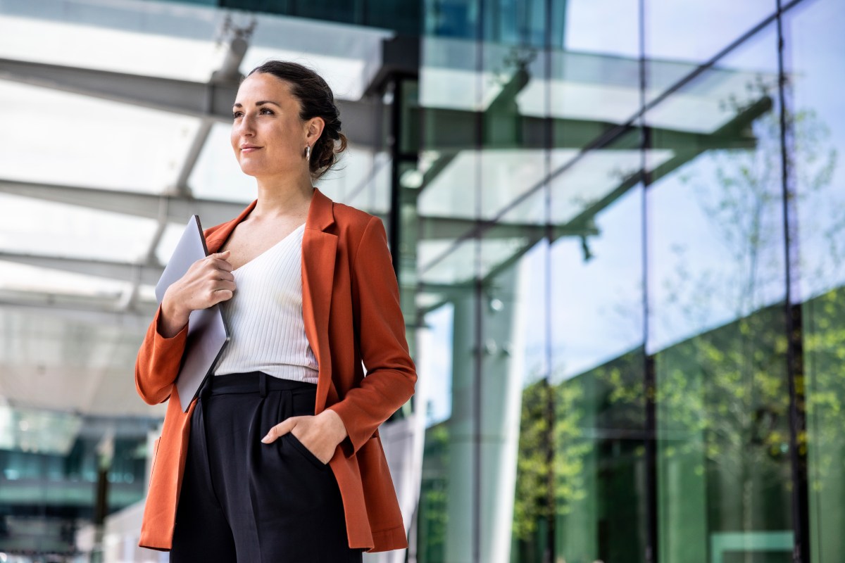 Geschäftsfrau hält Laptop vor Bürogebäude unter dem Arm.