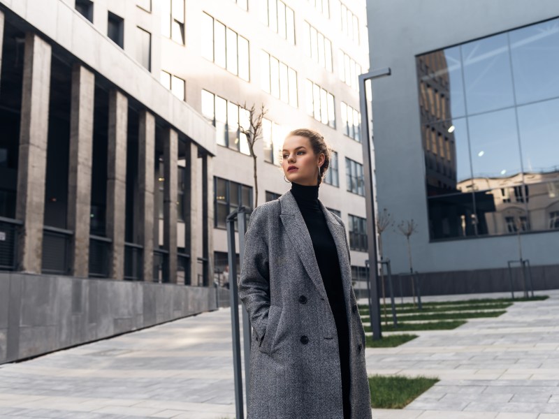 Mädchen im grauen Mantel vor einem Bürokomplex.