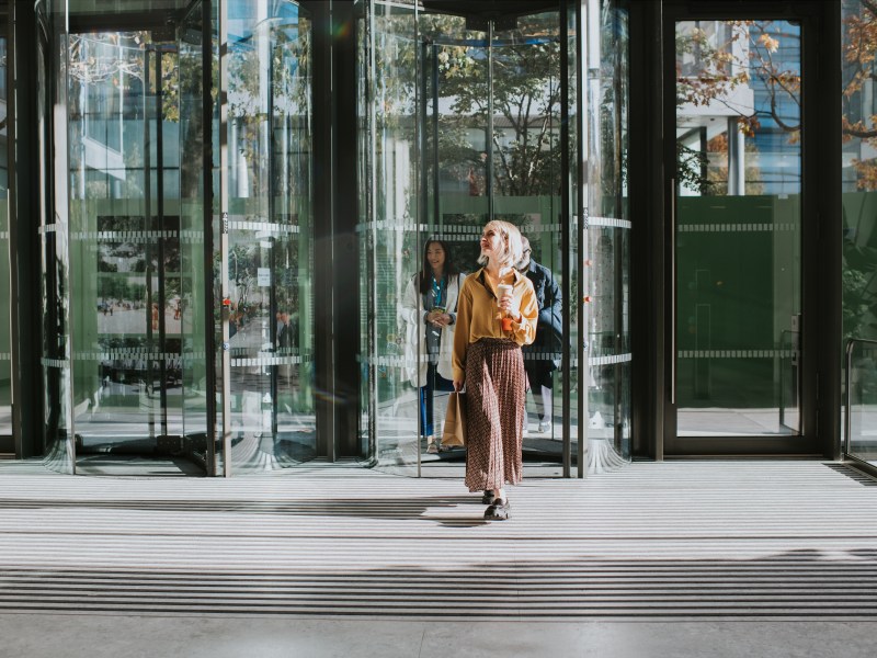 Eine Frau geht durch eine Drehtür in ein Gebäude.