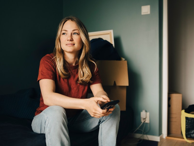 Frau sitzt auf Umzugskarton in Wohnung