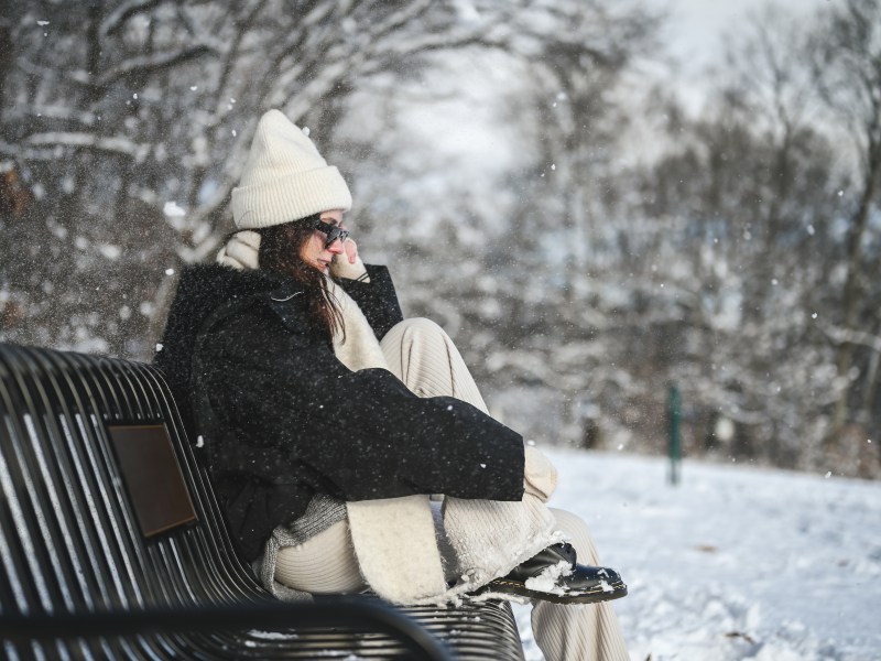 Frau sitzt im Schnee auf einer Bank mit Cordhose
