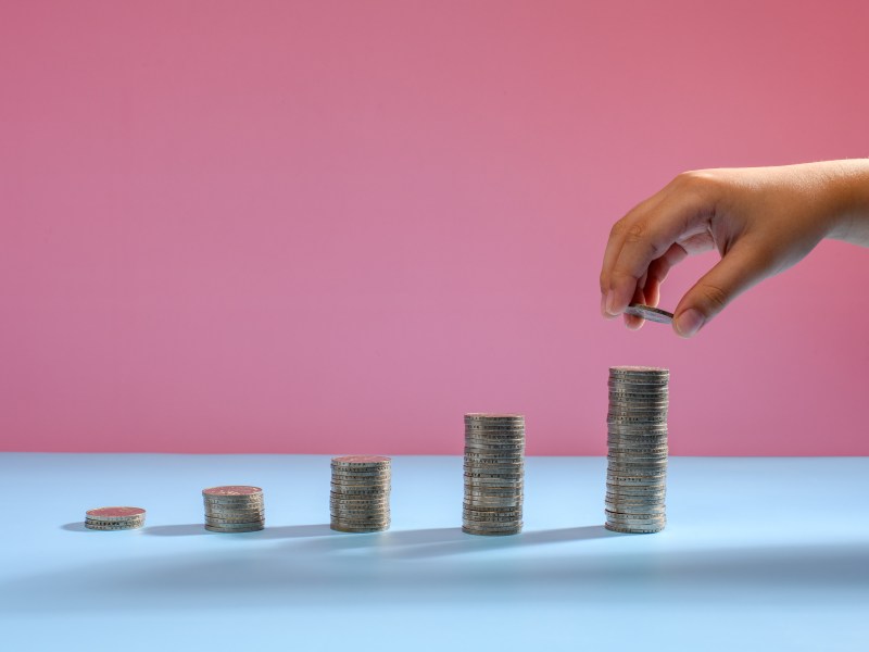 Geldmünzen als Diagramm angeordnet, wobei ein Junge die Hand hält und einen Stapel Geldmünzen auflegt