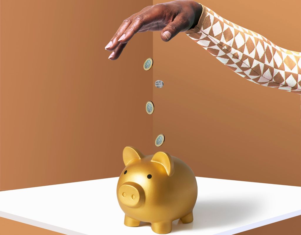 Eine Hand wirft M&uuml;nzen in ein goldenes Sparschwein.