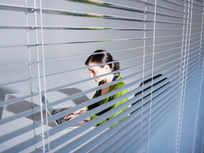 Junge Frau mit Laptop, Blick durch Fensterrollo.