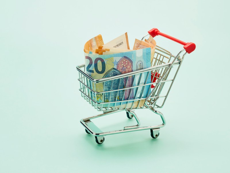 Stillleben mit Einkaufswagen und Euro-Scheinen auf türkisfarbenem Hintergrund