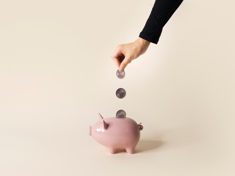 Eine Frauenhand wirft Münzen in ein Sparschwein.