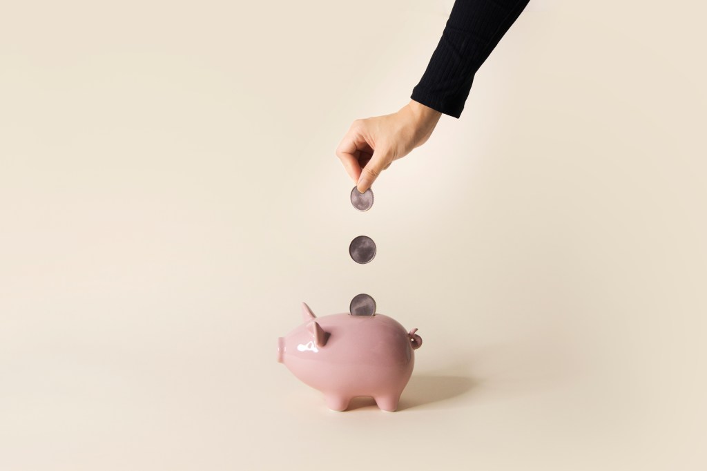 Eine Frauenhand wirft Münzen in ein Sparschwein.