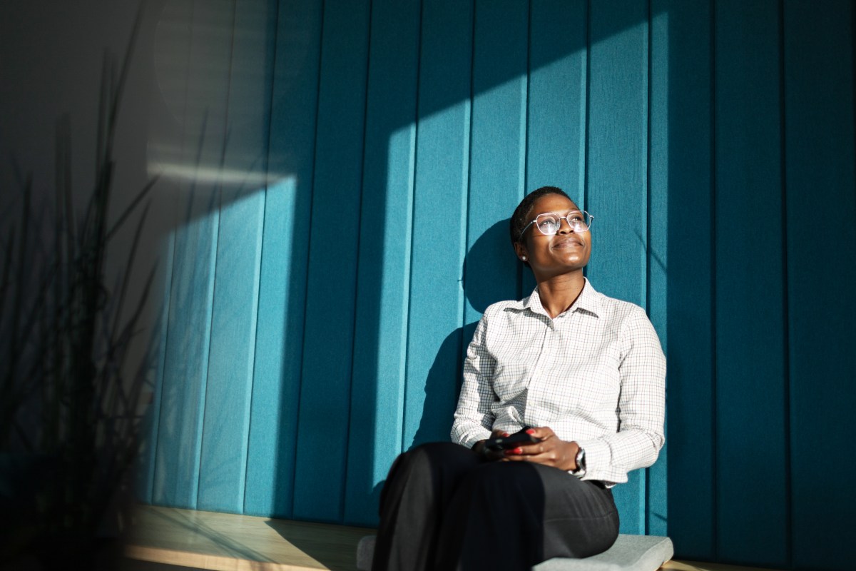 Junge erwachsene schwarze Frau sitzt lächelnd und entspannt im Büro.