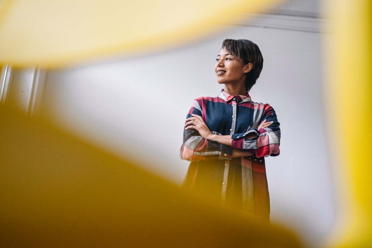 Eine Frau steht im Büro mit verschränkten Armen.