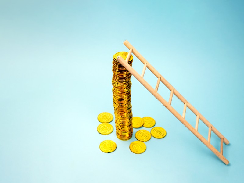 gestapelte Münzen. Eine kleine Leiter ist daran angelehnt.