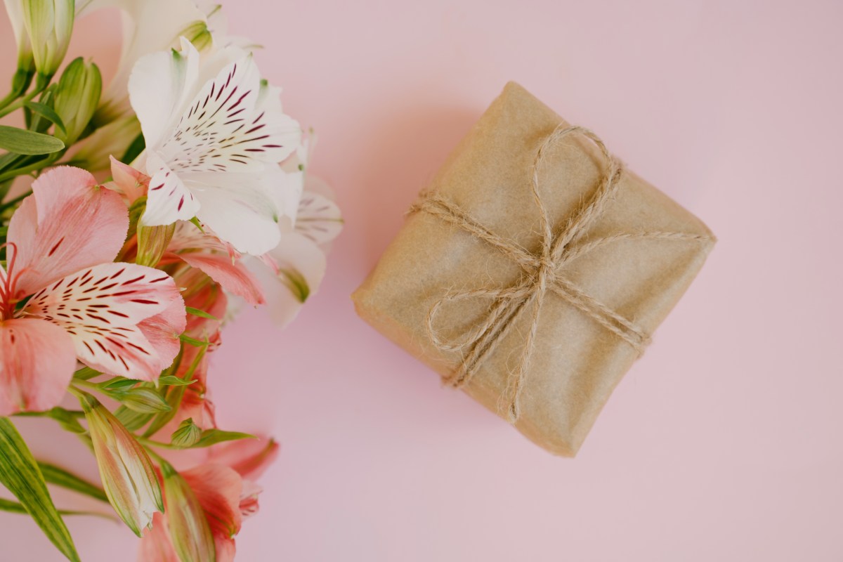 Bunte rosa und weiße Alstroemeria-Blüten und Geschenkbox mit braunem Kraftpapier auf rosa Hintergrund.