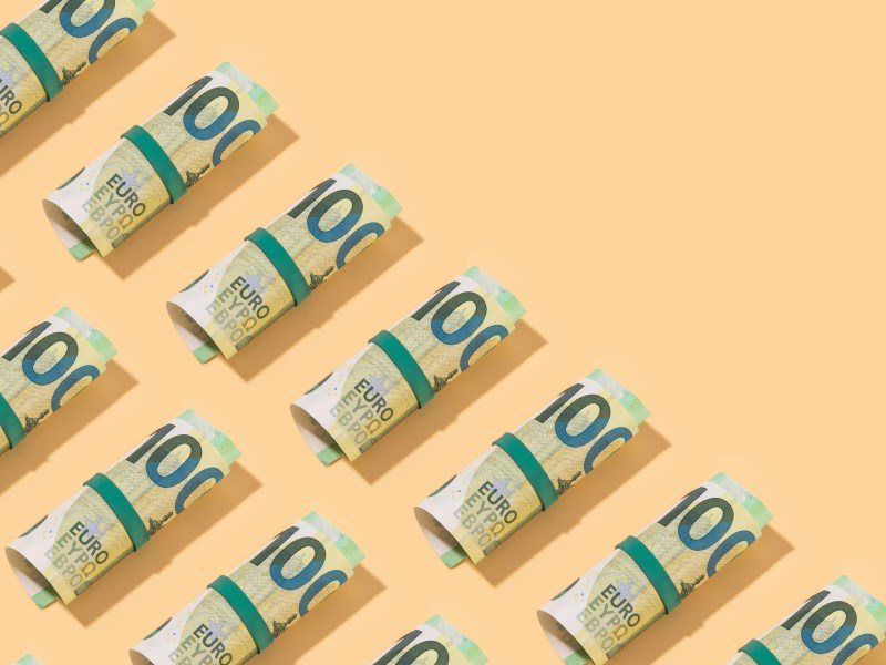 Rolle von Hundert-Euro-Scheinen auf orangenen Hintergrund.