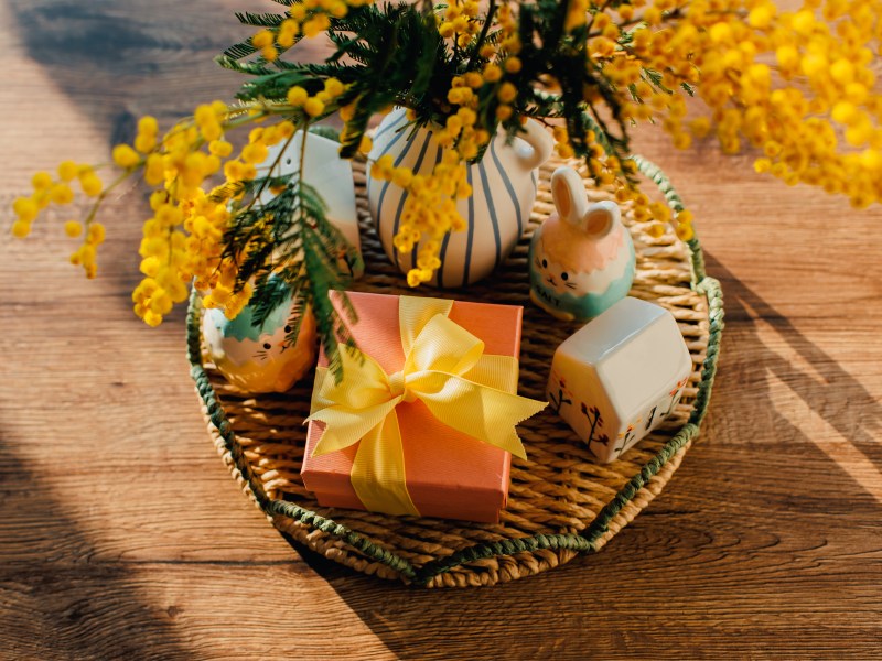 Mimosenblüten in der Vase, kleine Keramikdekor und ein Geschenk auf einem Tablett auf dem Holztisch.