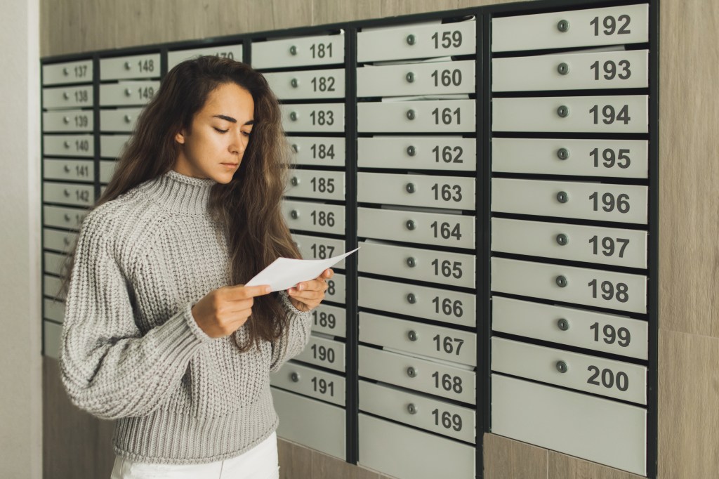 Frau liest einen Brief vor den Briefkästen ihres Wohnhauses.
