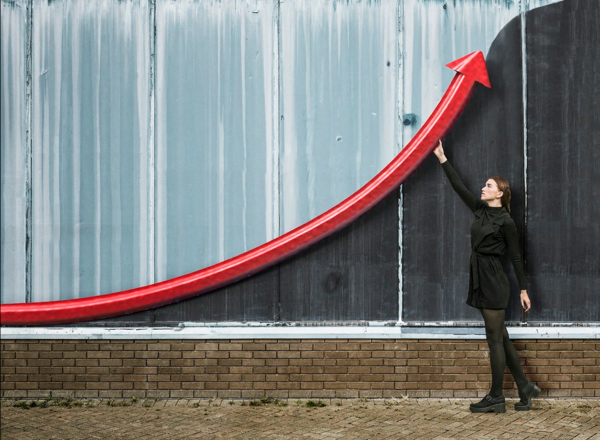 Eine junge Frau hält einen Pfeil an eine Wand, um Wachstum anzuzeigen.