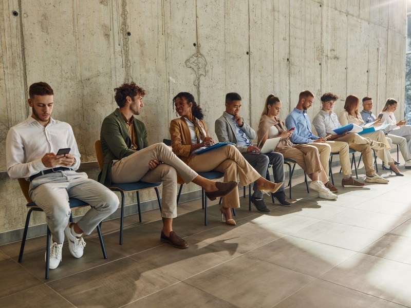 Große Gruppe von Bewerber:innen wartet in einem Flur auf ein Vorstellungsgespräch