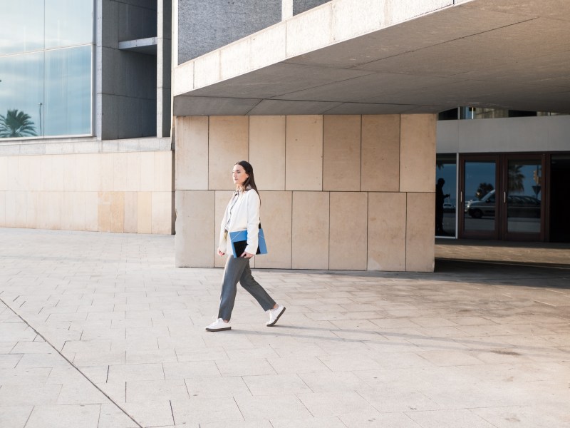 Eine Frau läuft mit Unterlagen vor einem Gebäudekomplex.