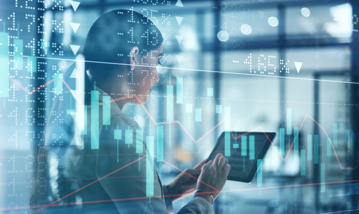 Eine Frau hält ein Tablet in der Hand. Um sie herum sind Börsenkurven.