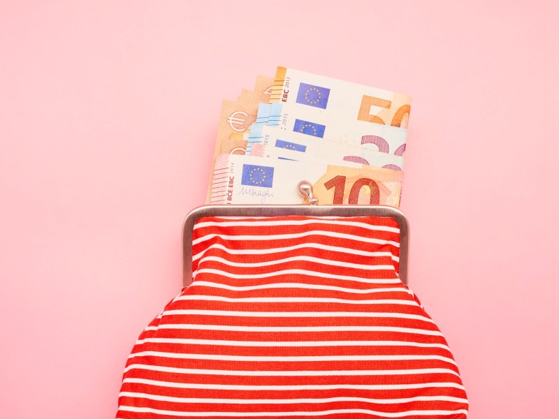 Aufnahme einer Brieftasche und Euro-Banknoten auf rosa Hintergrund.