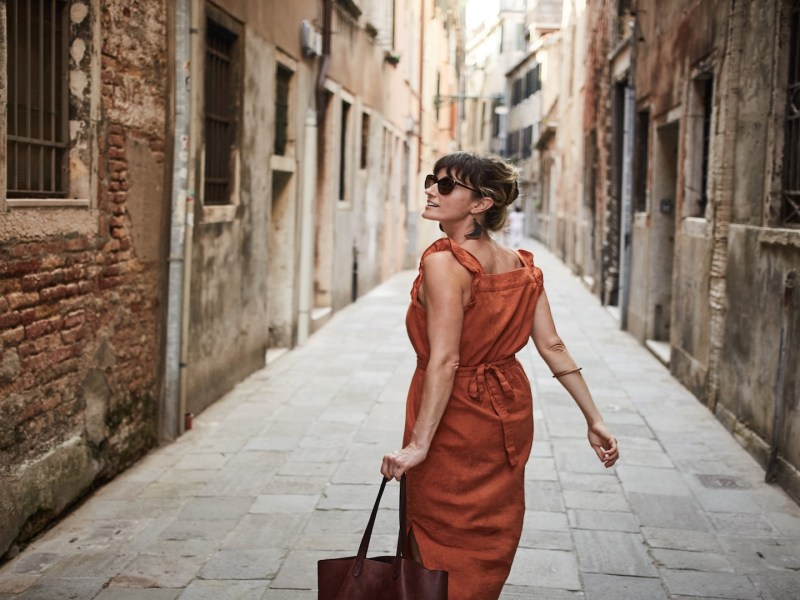 Eine Frau mit Sonnenbrille geht durch die Gassen einer italienischen Stadt.