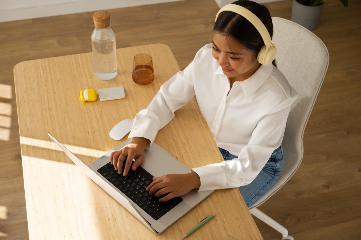 Junge Frau mit Kopfhörern arbeitet zu Hause mit Laptop am Tisch.