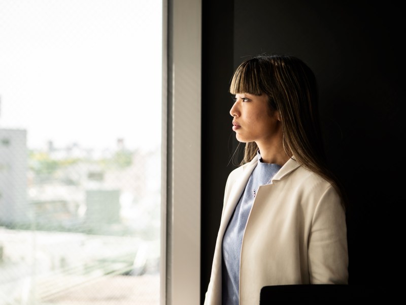 Eine Frau im beigen Anzug schaut im Büro aus dem Fenster.