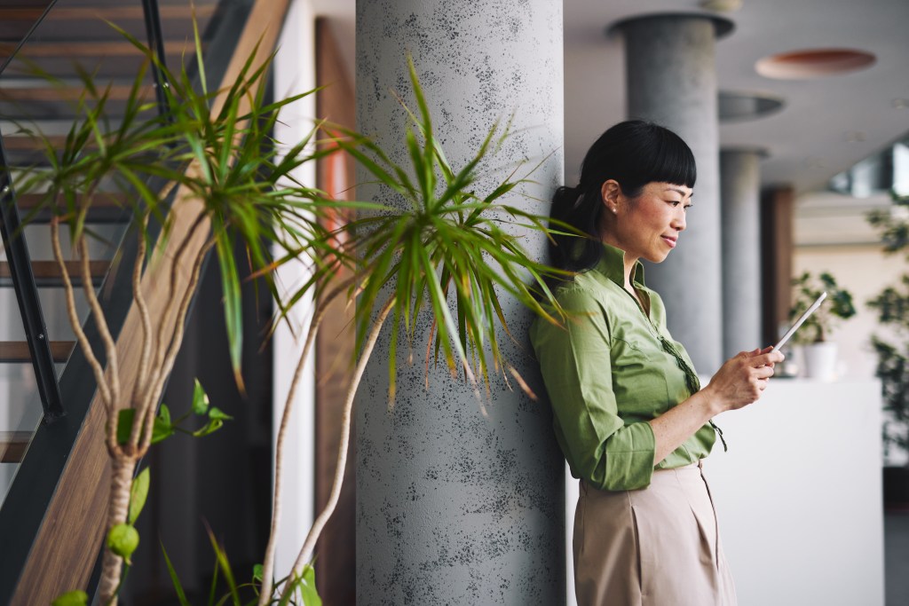 Gesch&auml;ftsfrau steht neben einer Betons&auml;ule und schaut auf ein Tablet.