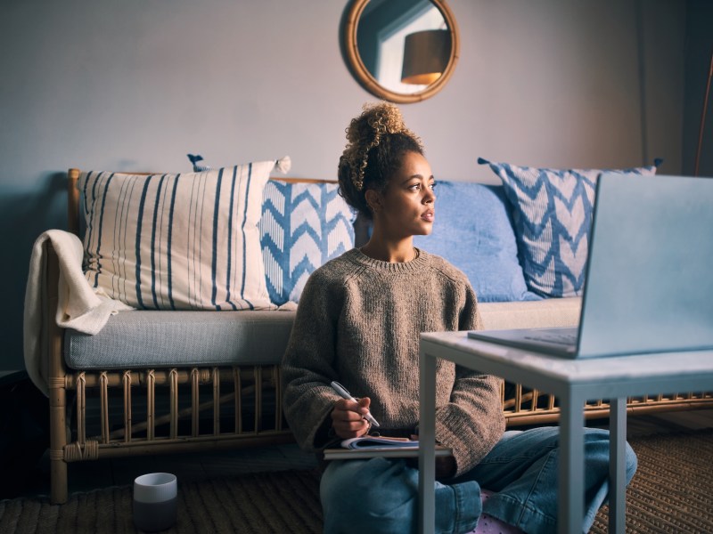 Junge Frau schreibt auf ihrem Sofa ein Journal.