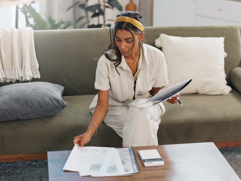 Eine Frau sitzt auf dem Sofa und bearbeitet Steuerunterlagen.