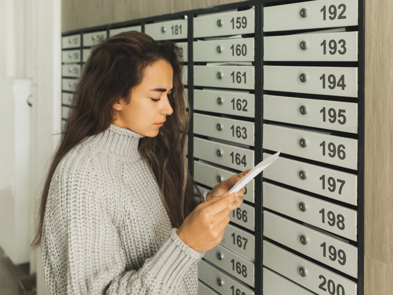 Junge Frau holt einen Brief aus dem Briefkasten.