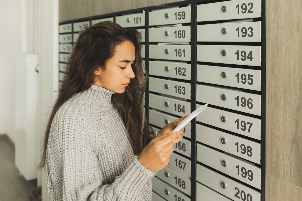Junge Frau holt einen Brief aus dem Briefkasten.