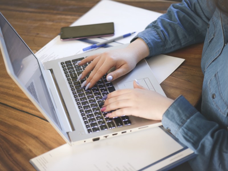 Eine Frau mit bunten Fingernägeln bearbeitet ihre Steuererklärung ab Laptop.