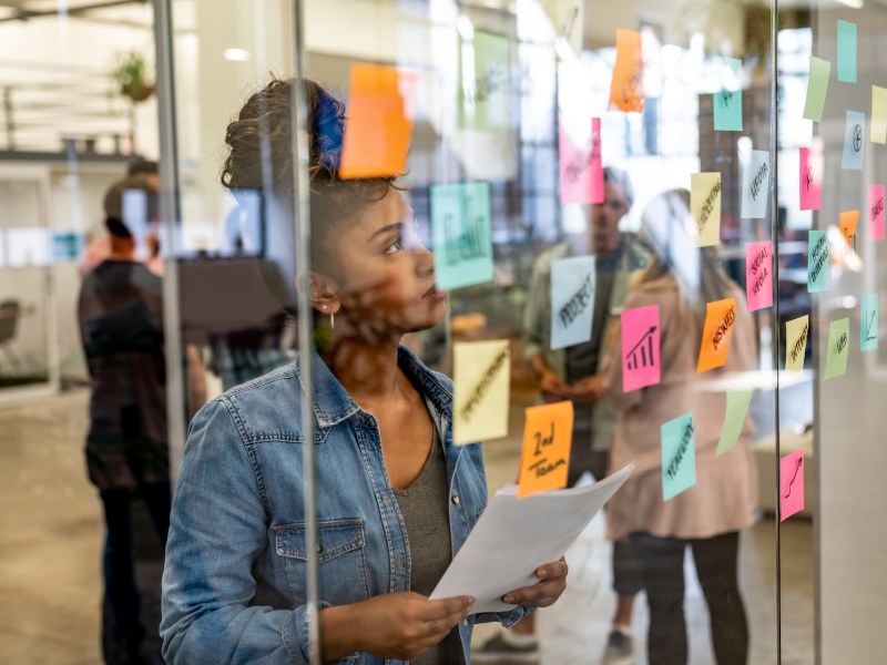 Porträt einer nachdenklichen Geschäftsfrau, die beim Brainstorming Haftnotizen verwendet.