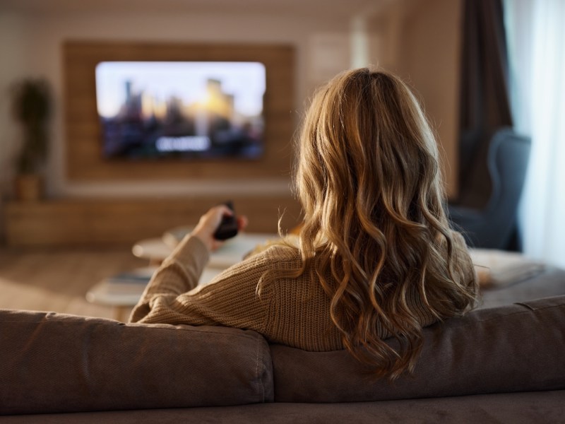 Eine Frau sitzt auf dem Sofa und schaut TV.