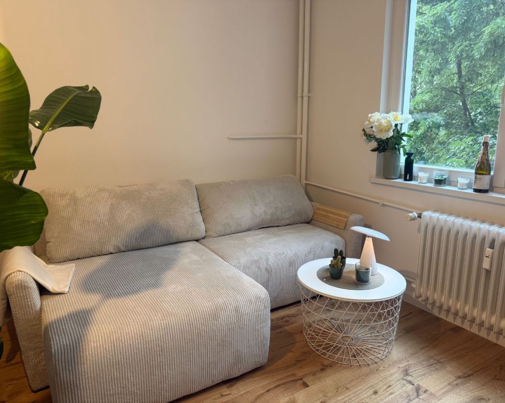 Ein Wohnzimmer mit einer beigefarbenen Cord-Couch und einem Beistelltisch mit einer Akku-Lampe.