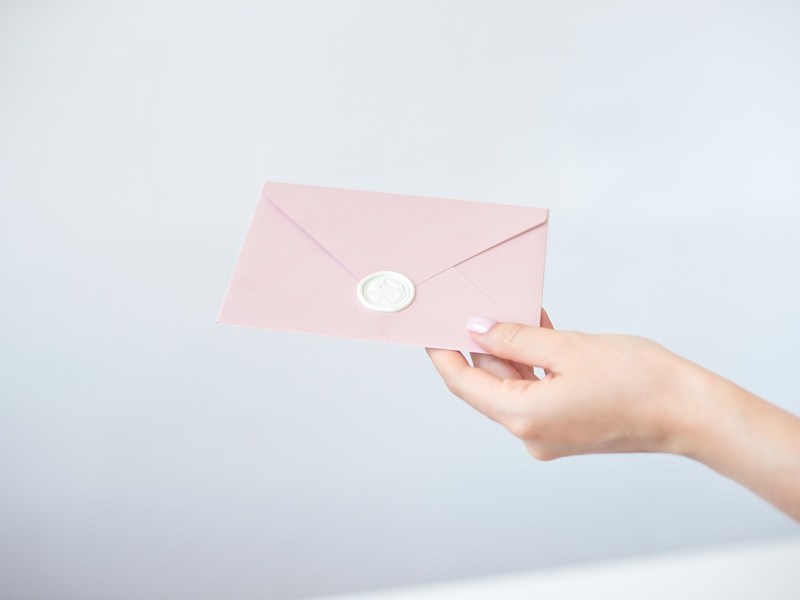 Eine Frau mit rosa Fingernägeln hält einen Rosinen Umschlag in der Hand.