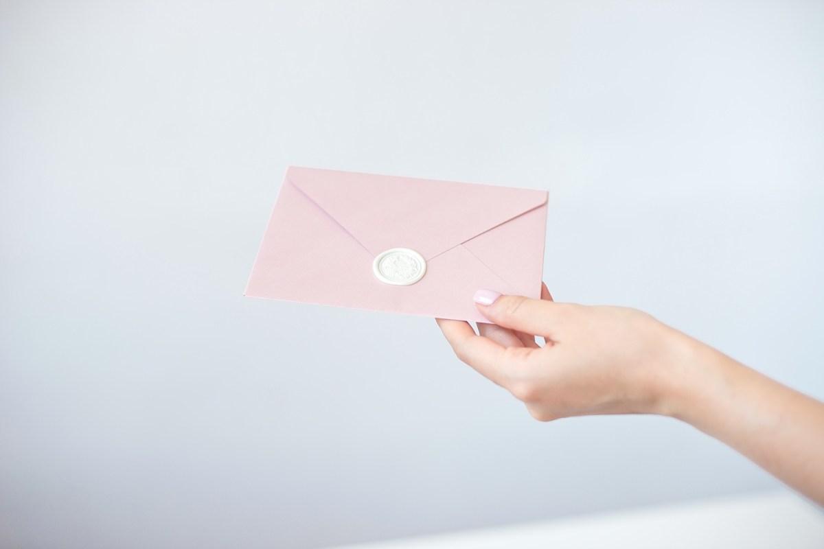 Eine Frau mit rosa Fingernägeln hält einen Rosinen Umschlag in der Hand.